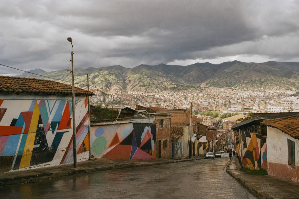 Heavy grey clouds building over green mountain ridges above a valley city in late afternoon with sunlit rooftops in the foreground