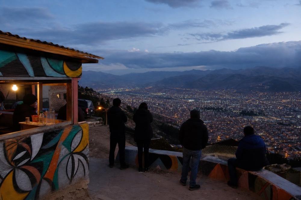 Hillside viewpoint terrace with a small drinks kiosk and low wall, visitors seen from behind looking across the valley