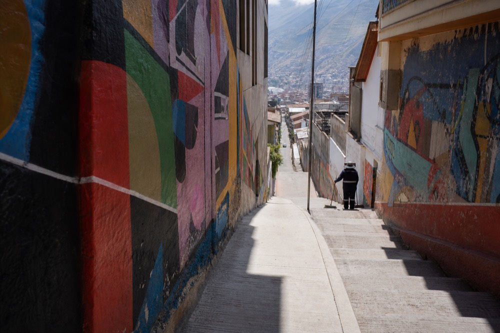 Early morning light on an almost empty painted stairway corridor, long shadows across the steps, a single street sweeper working at the far end