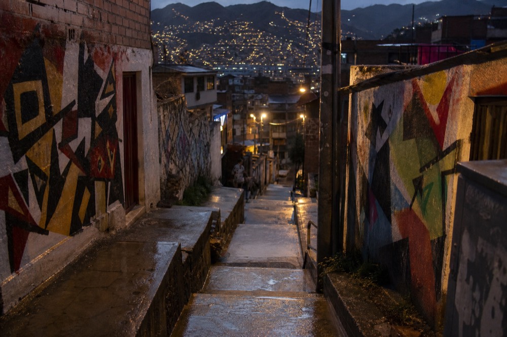 Rain-wet concrete steps climbing between hillside houses at dusk, puddles reflecting scattered window lights, no people in the frame